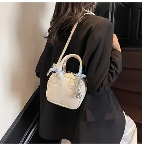 Cream mini bowling bag detail featuring lace bow accents and silver bear charm charm