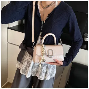 Detail of cream leather square handbag featuring silver buckle and woven charm accessory