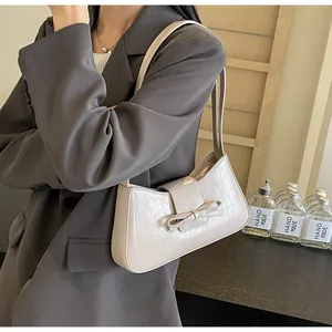 Close-up of cream underarm bag with bow detail and cracked leather texture on a model