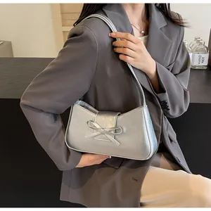 Detail of silver metallic baguette bag featuring a chic leather bow and smooth texture