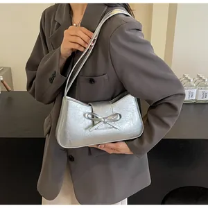 Silver baguette bag with bow detail worn over the shoulder with a dark gray suit