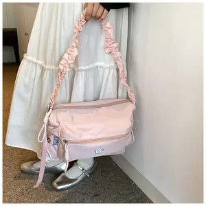 Détail du sac bandoulière en nylon rose avec bandoulière plissée et emblème d'ours