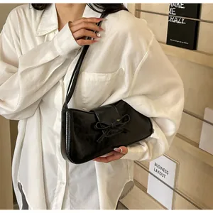 Detail of a black faux leather underarm bag featuring a stylish 3D bow and glossy finish