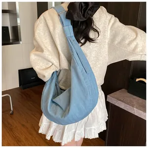 Détail d'un grand sac hobo en denim bleu avec bandoulière réglable porté par un mannequin