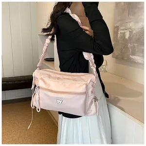 Détail du sac bandoulière rose clair en nylon avec badge d'ours et sangle à volants