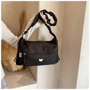 Détail d'un sac bandoulière en nylon noir avec bandoulière froncée et patch ours