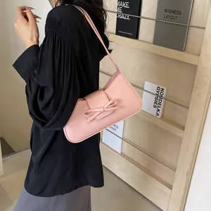 Pink matte leather shoulder bag with bow detail shown on model with black shirt