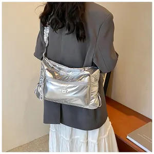 Détail d'un sac bandoulière argenté métallisé avec emblème d'ours et texture plissée