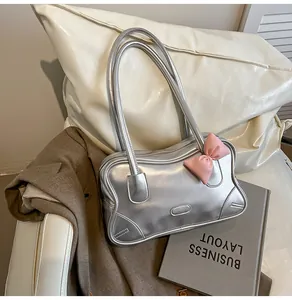 Silver shoulder bag detail with a pink leather bow on a couch with a brown blazer