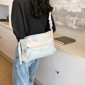 Sac bandoulière blanc en nylon avec sangle plissée et détail d'ours dans un intérieur