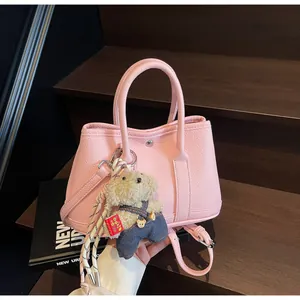 Detail view of pink lychee leather bucket bag with cute teddy bear charm on wooden steps
