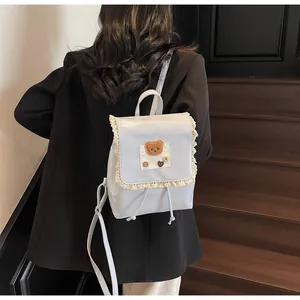 Detail eines hellblauen Lederrucksacks mit Spitzenbesatz und Plüschbär-Dekoration