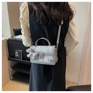 Detail of grey patterned crossbody bag with dog charm and metal lock in a home setting