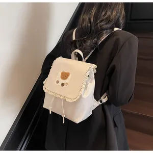Detail eines cremeweißen Rucksacks mit Spitzenbesatz, Plüschbär und Herzschnallen