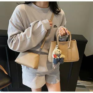 Detail of khaki lychee leather tote bag and crossbody set with teddy bear charm accessory