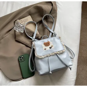 Detail eines hellblauen Rucksacks mit Spitzenbesatz, Plüschbär und Kordelzugverschluss