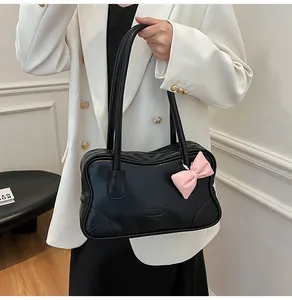 Close-up of black leather tote bag with wavy edges and a pink bow charm on a model