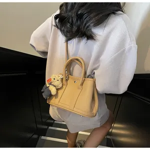 Detailed macro view of khaki pebbled leather bucket bag with cute bear charm and metal feet
