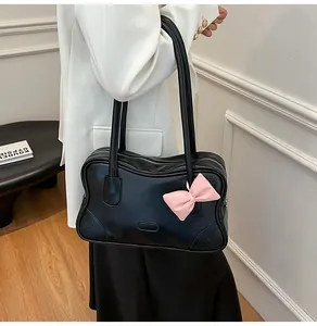 Detail of black vintage PU tote bag with pink bow charm shown on a white blazer
