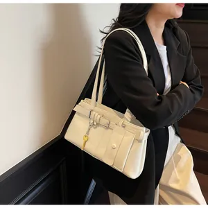 Detail of cream white shoulder bag with decorative buckle and yellow key pendant accessory