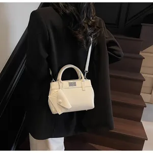 Detail of white leather handbag featuring a mini triangle charm and silver metal clasp