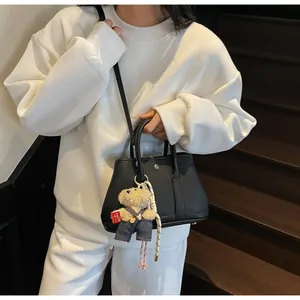 Detail of black pebbled leather bucket bag with cute teddy bear charm on white outfit