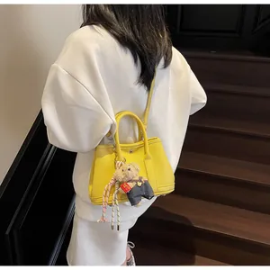 Bright yellow bucket bag with teddy bear charm on model wearing white hoodie