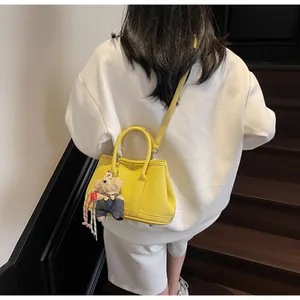 Detail of yellow pebbled leather bucket bag with a cute bear charm and shoulder strap