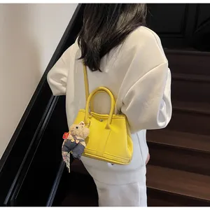 Detail of a bright yellow textured leather tote bag with a cute bear charm on a model