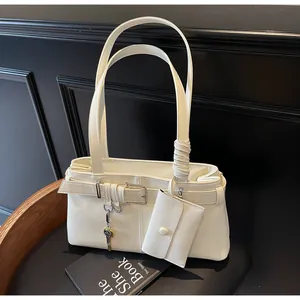 Detail of cream-white leather shoulder bag with key charm and small pouch on black seat