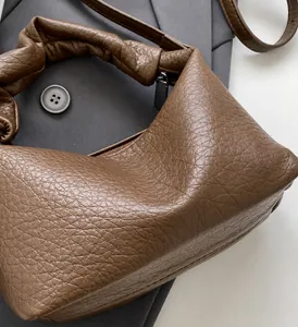 Close-up of brown leather bag with pleated handle design and metallic zipper detail