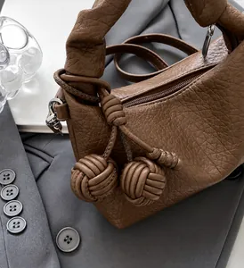 Macro view of brown lychee pattern leather handbag with creative braided ball charms