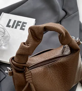 Detailed close-up of dark brown lychee leather handbag with pleated knotted handle