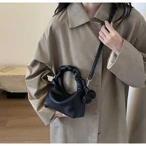 Detail of black pebbled leather bag with pleated handle and woven charms on a trench coat