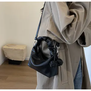 Detail of black textured dumpling bag with knot handle and adjustable crossbody strap