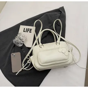 Detailed view of cream pillow bag with embossed bow, leather strap, and metal buckles