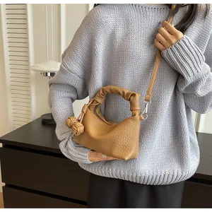 Detail of tan lychee grain leather handbag with knotted handle and woven ball charm