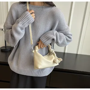 Detail of cream crossbody bag featuring a knotted handle and woven ball charm accessory