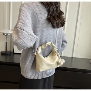 Close-up of beige dumpling bag with litchi texture and knotted handle worn on shoulder