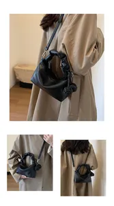 Detail of black pebbled leather dumpling bag featuring pleated handles and woven charms