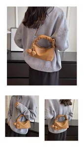 Detail of brown faux leather hobo bag featuring pleated handles and braided ball pendants