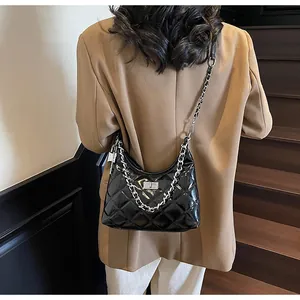 Detail of black quilted patent leather bag with silver chain strap on model's shoulder