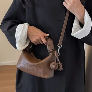 Dark brown leather dumpling bag with knot handle and woven pendant crossbody style