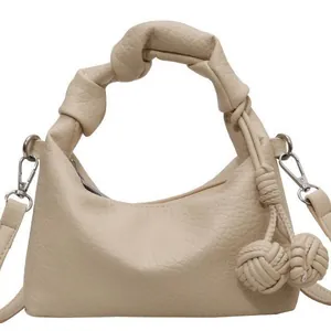 Chic beige dumpling bag with knotted handle and decorative woven pendants
