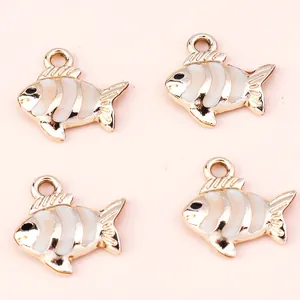 Close-up of four gold and white fish-shaped alloy charms for DIY jewelry making