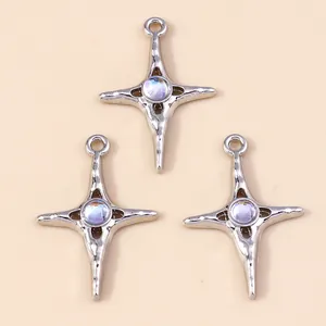 Three silver-tone star cross pendants with iridescent central gems on beige background