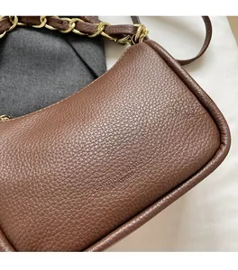 Gros plan du cuir marron grainé et de la bandoulière en chaîne dorée du petit sac carré