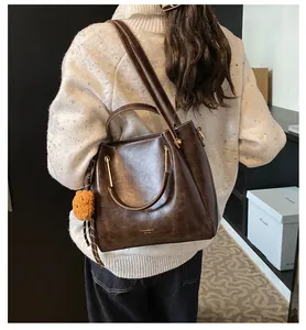 Detail of dark brown leather tote bag with metal handle and yellow pompom charm accessory