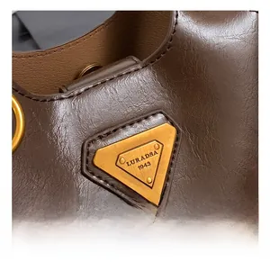 Close-up of golden triangular metal logo plate on brown oil-wax leather shoulder bag