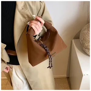 Detalle de bolso de hombro marrón con asa anudada y cuerda trenzada sobre una gabardina